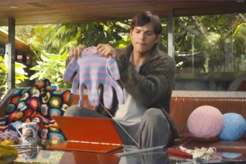 Still shot of Lenovo commercial featuring Ashton Kutcher holding up a knitted onesie for a baby octopus