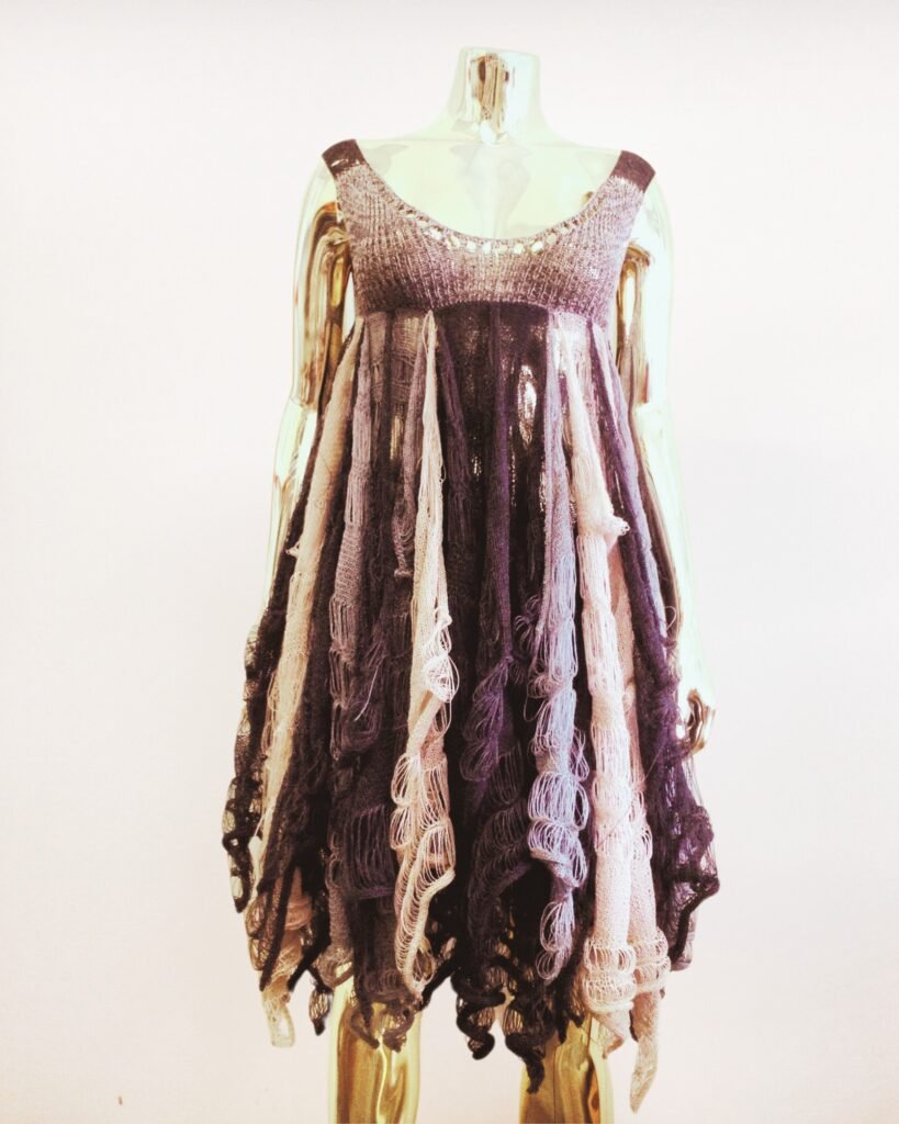 Gold mannequin wearing a knit babydoll dress featuring many layers of textured lightweight knit pieces