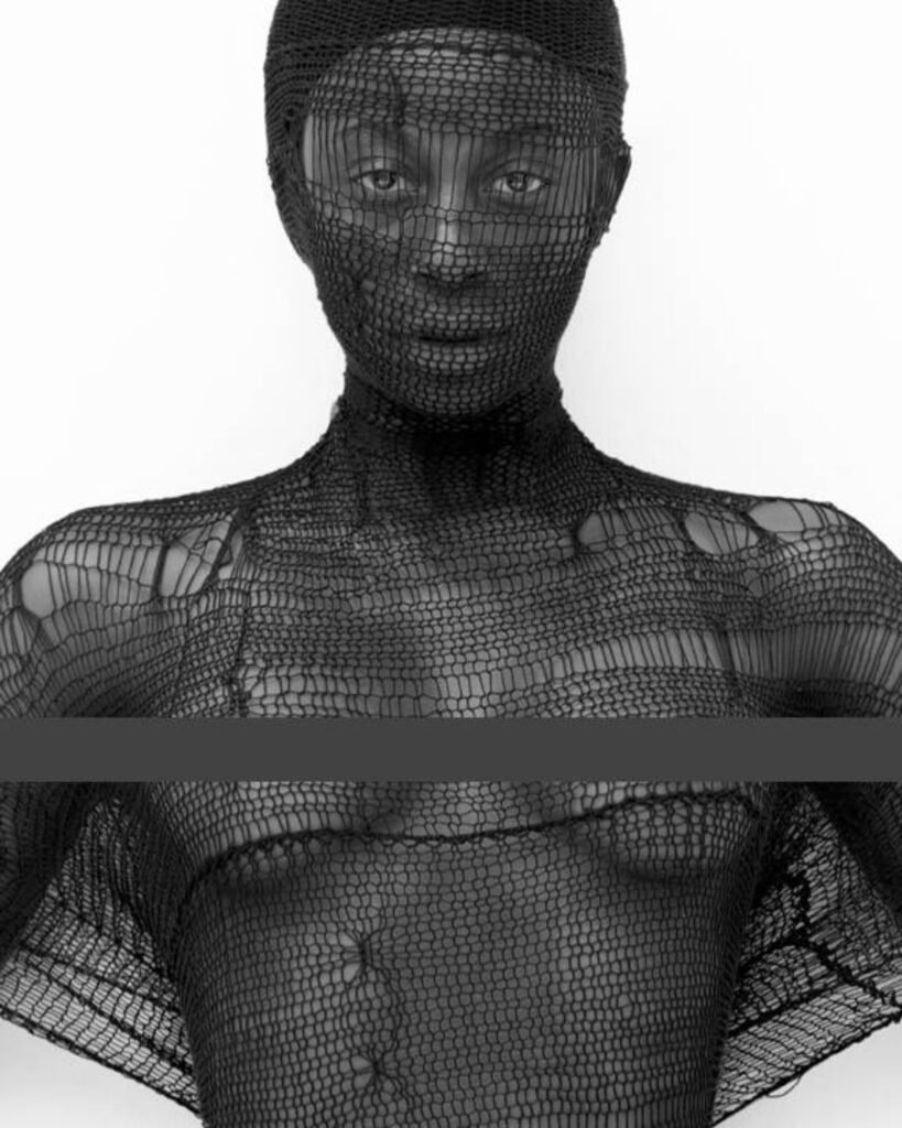 Model wearing a black shredded knit shawl covering her face and upper body