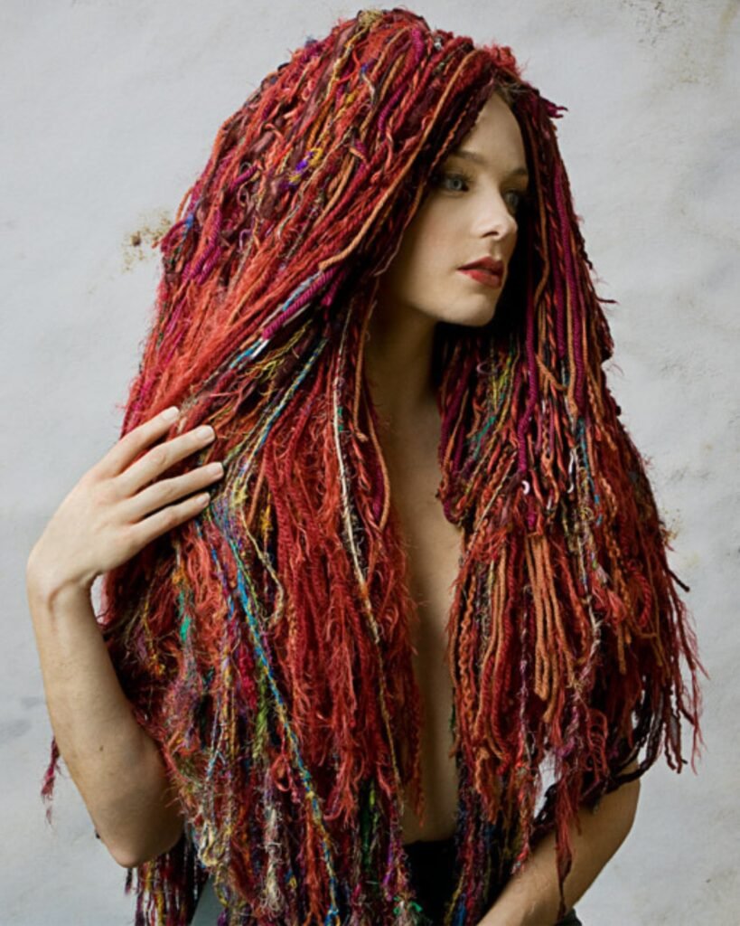 Model wearing a wig made of numerous yarns in shades of red